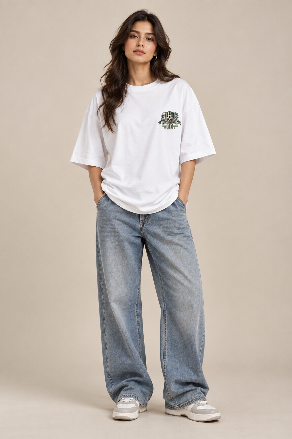 White oversized football T-shirt with a small green and cream soccer crest graphic on the chest styled with baggy pants.