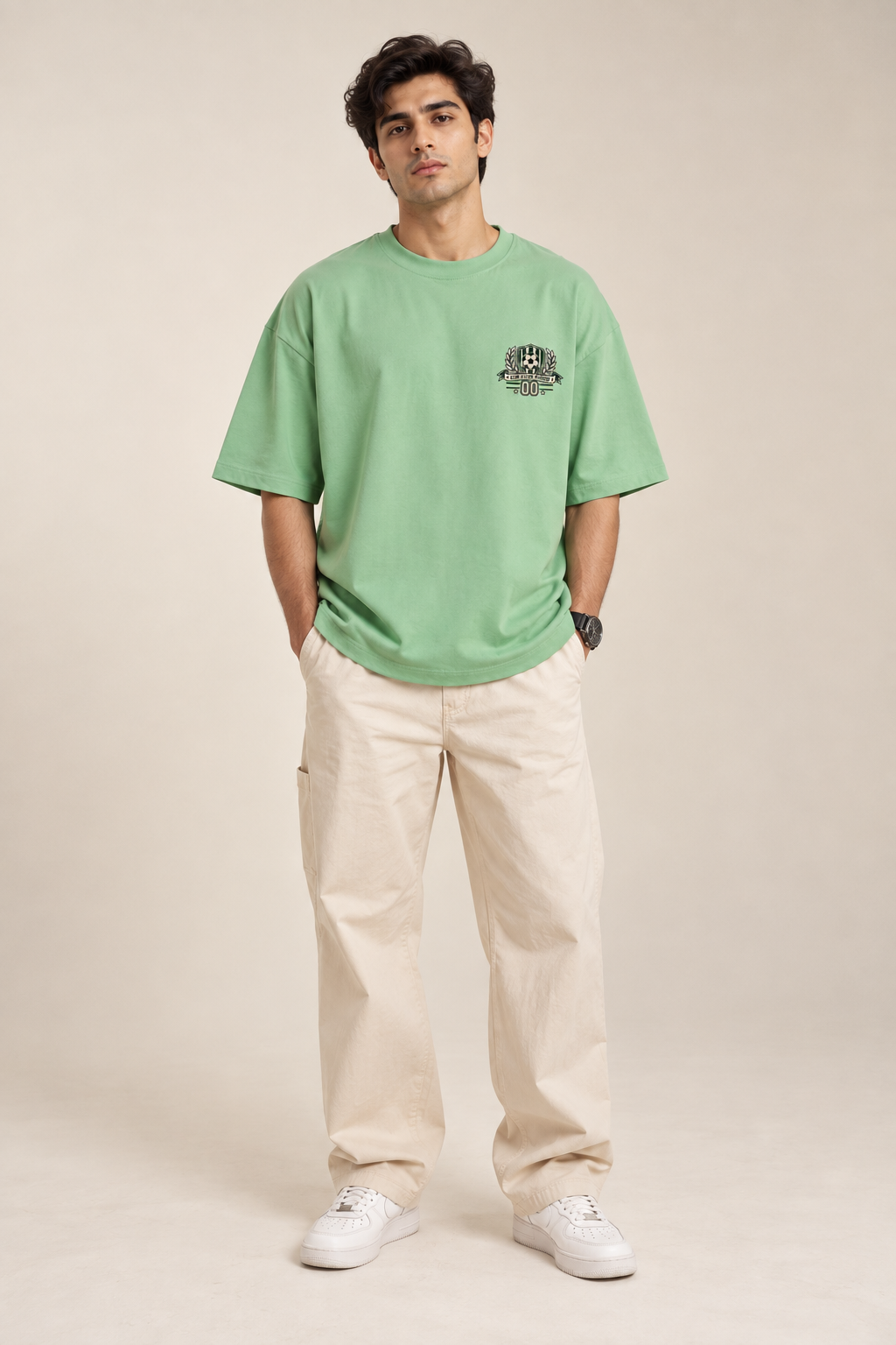 Jade green oversized football T-shirt with a small green and cream soccer crest graphic on the chest styled with baggy pants.