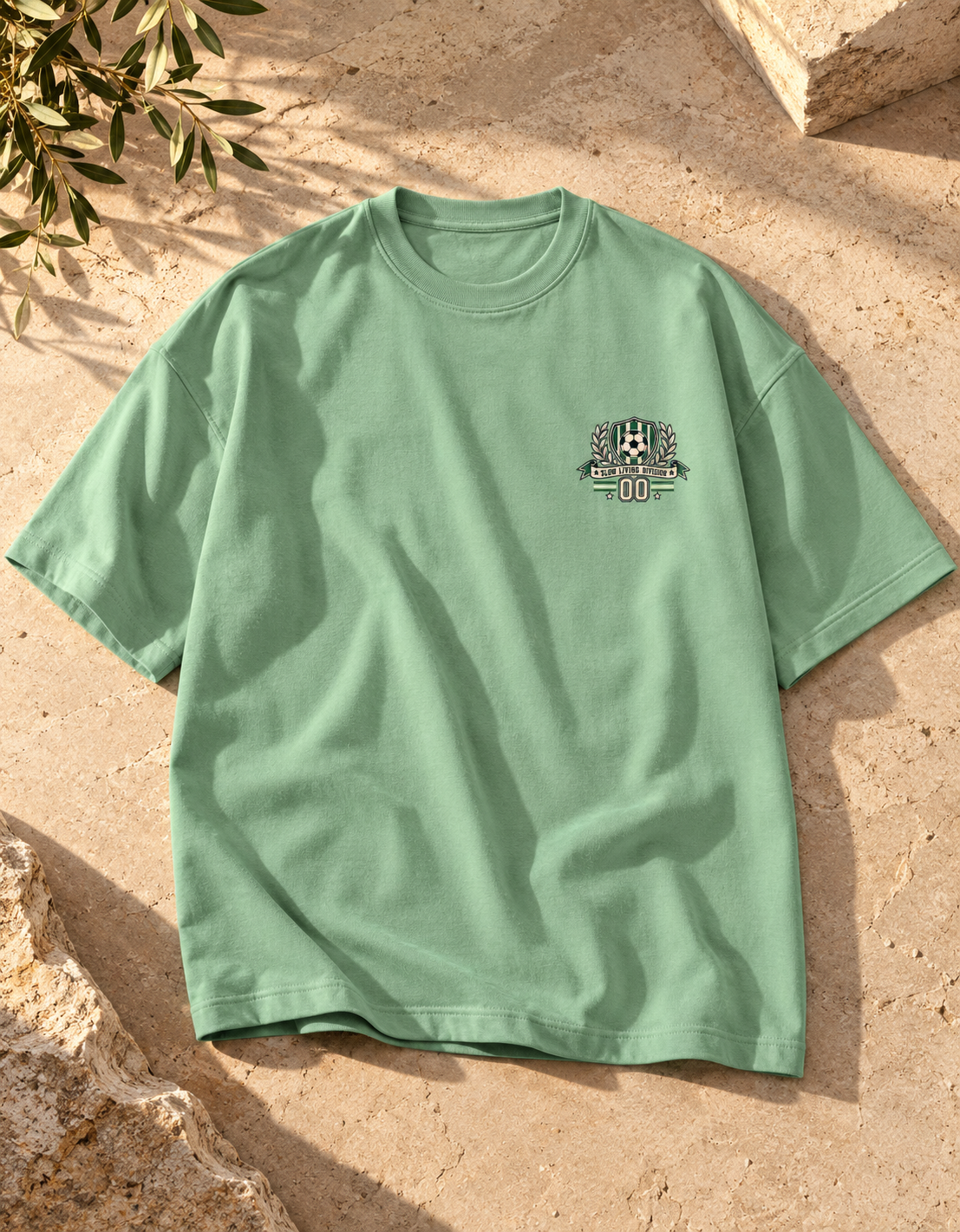 Jade green oversized football T-shirt with a small green and cream soccer crest graphic on the chest.