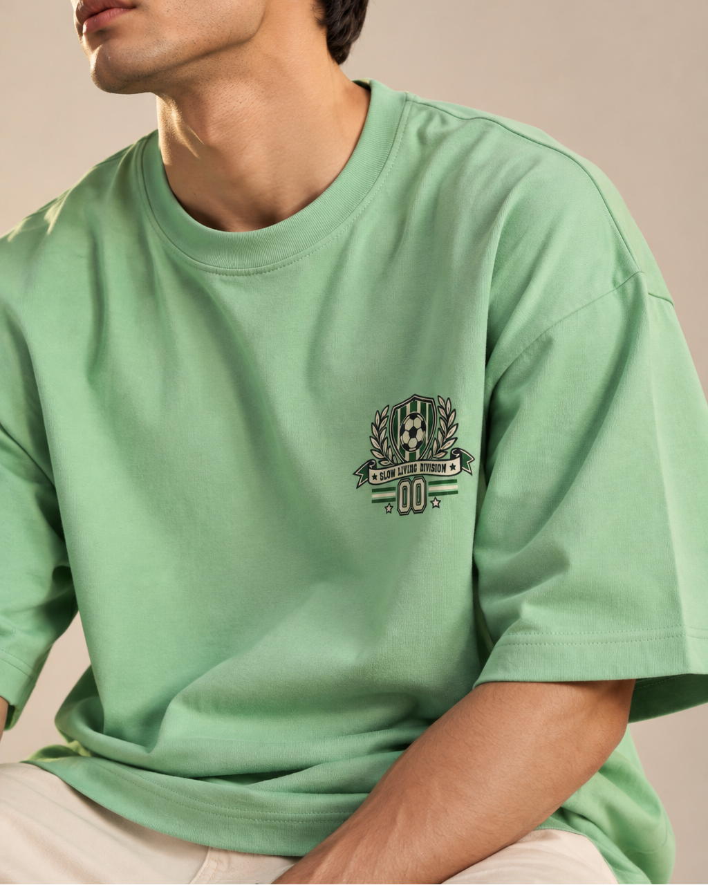 Jade green oversized football T-shirt with a small green and cream soccer crest graphic on the chest.