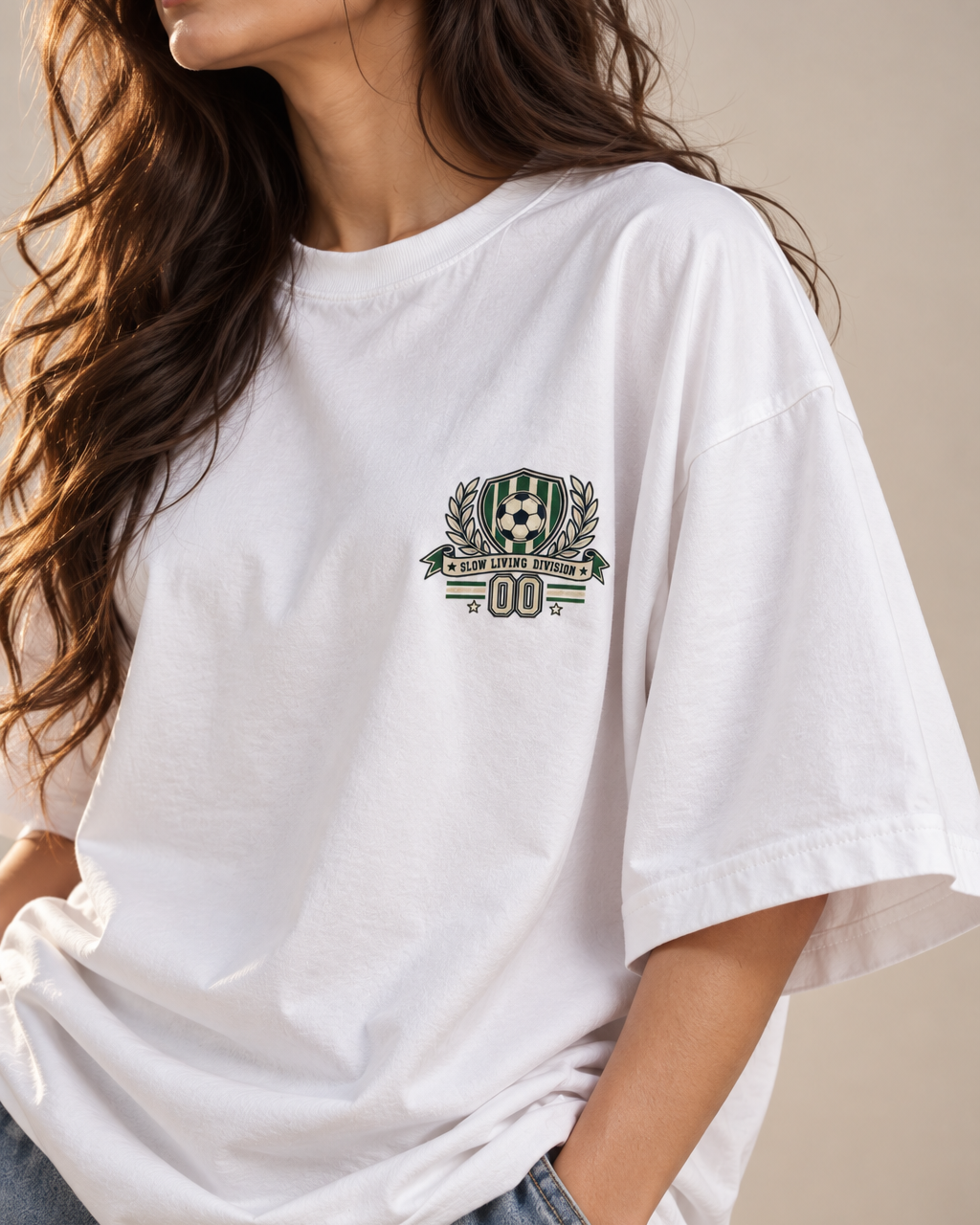 White oversized football T-shirt with a small green and cream soccer crest graphic on the chest.