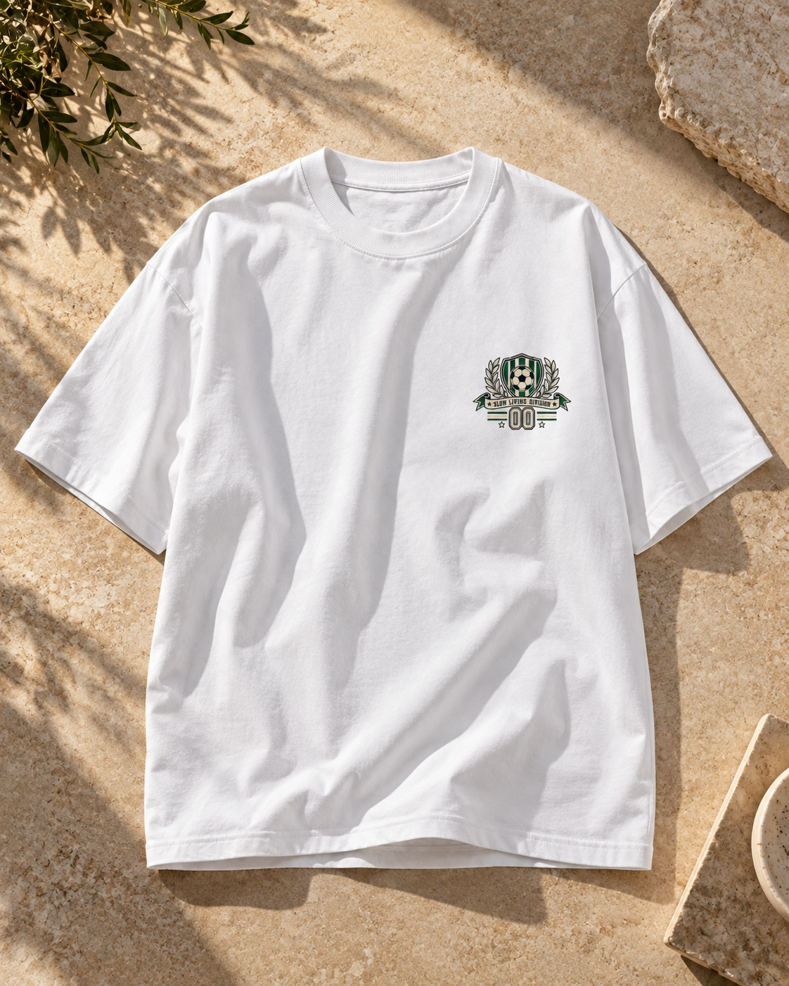 White oversized football T-shirt with a small green and cream soccer crest graphic on the chest.