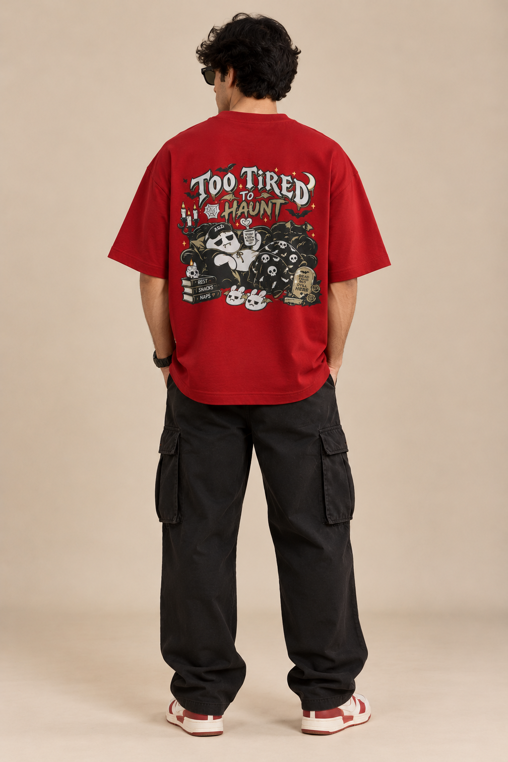Red oversized Halloween T-shirt featuring “Too Tired to Haunt” lettering, sleepy ghost artwork, bats, skulls, candles and gothic details on the back styled with baggy pants.
